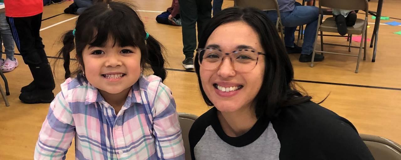 A mom and her young daughter smile at the camera.